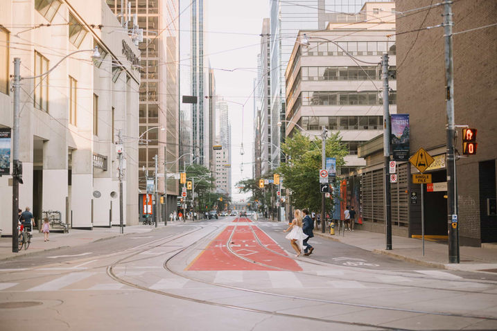 A couple holds hands while crossing the streetcar tracks on an empty street in downtown Toronto, with skyscrapers lining the road.