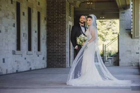A romantic full-length portrait of a bride and groom standing together beneath the grand stone arches of The Arlington Estate pavilion.