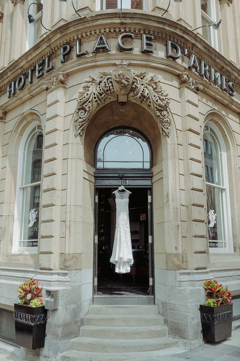 A beautiful strapless wedding gown hanging elegantly in the grand stone archway entrance of a historic Toronto venue.