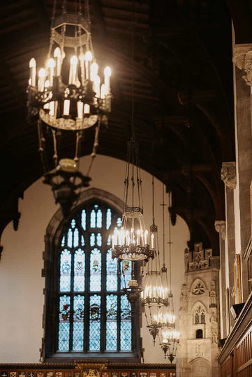 Low-angle architectural perspective focusing on vintage wrought iron chandeliers hanging from the timber-beamed ceiling of the Great Hall at Hart House.