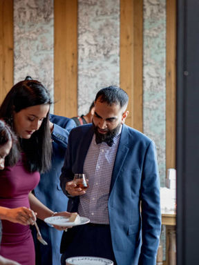 A documentary wedding photograph of guests chatting and enjoying drinks during a relaxed indoor-outdoor cocktail reception.