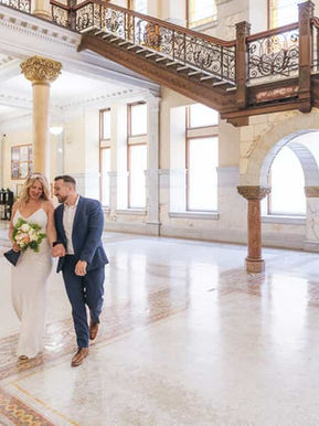 Bride and groom walking through the bright, sunlit marble foyer of Old City Hall during their wedding portrait session.