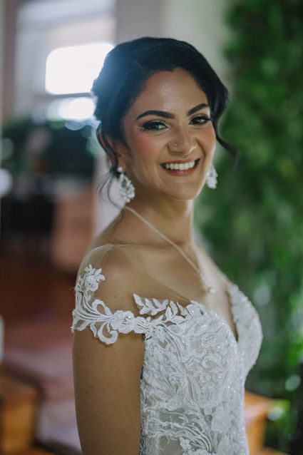 A bright close-up portrait of a beautifully smiling bride wearing an off-the-shoulder lace wedding dress.
