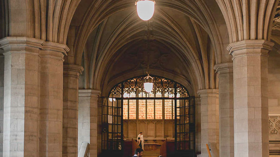 Bride and groom ascend stairs in grand hall with vaulted ceilings. Bride in white gown; photographer captures moment. Elegant and historic.