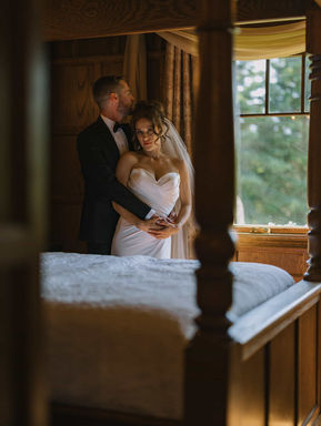 A moody, wide-angle shot of a couple exchanging vows beneath a rustic wooden arch deep inside a shaded forest grove.