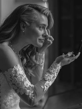 Close up black and white portrait of a bride looking into a mirror while emotionally applying makeup, Close up black and white portrait of a bride looking into a mirror while emotionally applying makeup, showing intricate lace details on her sleeve. intricate lace details on her sleeve.