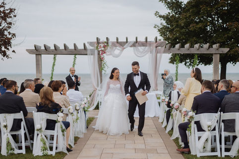 Bride and groom walking down the outdoor aisle under a wooden pergola during a waterfront ceremony at Edgewater Manor.