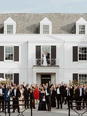 A wide outdoor photograph of an entire wedding guest list gathered on the terrace of a classic white estate venue.