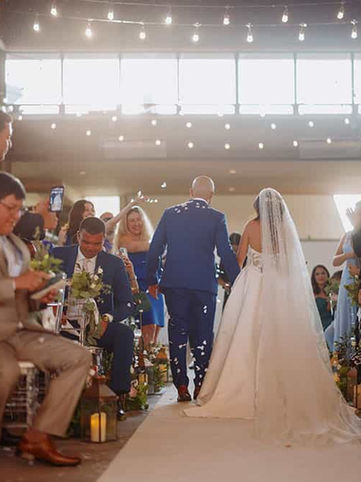 Documentary-style ceremony photography capturing the bride's entrance through a sun-drenched aisle filled with guests.