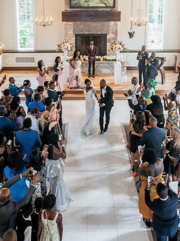 High-angle interior documentary photograph capturing a full wedding ceremony inside the bright, sun-drenched timber-framed chapel hall at Ancaster Mill with guests looking on.