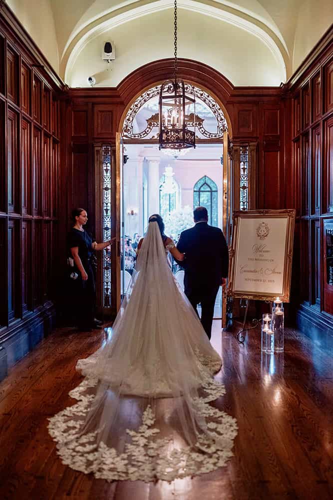 Bride with a long flowing train entering a grand, wood-paneled room for an elegant wedding at Casa Loma in Toronto