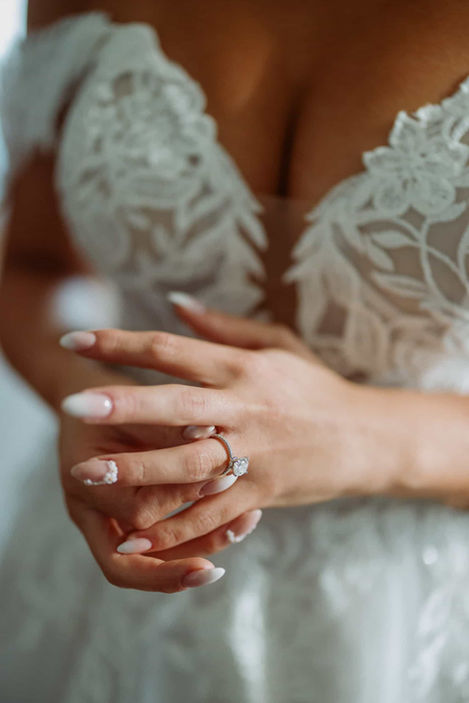 Close-up of bride's hand with engagement ring and delicate manicure against lace fabric
