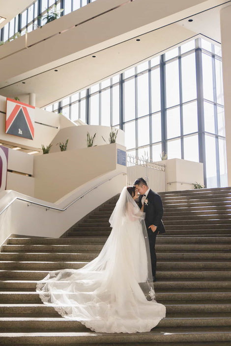 Romantic creative shot of a couple sharing a kiss on a grand indoor staircase with soft, diffused light from large windows.