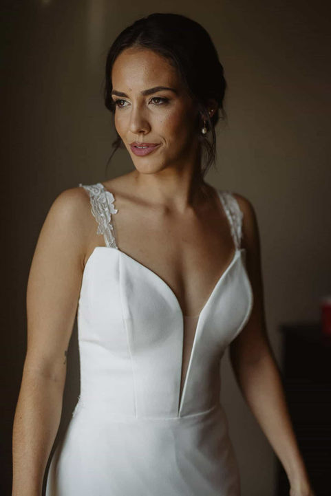 A bride modeling a modern, minimalist wedding dress with a deep V-neckline in a moody, dramatically lit room.