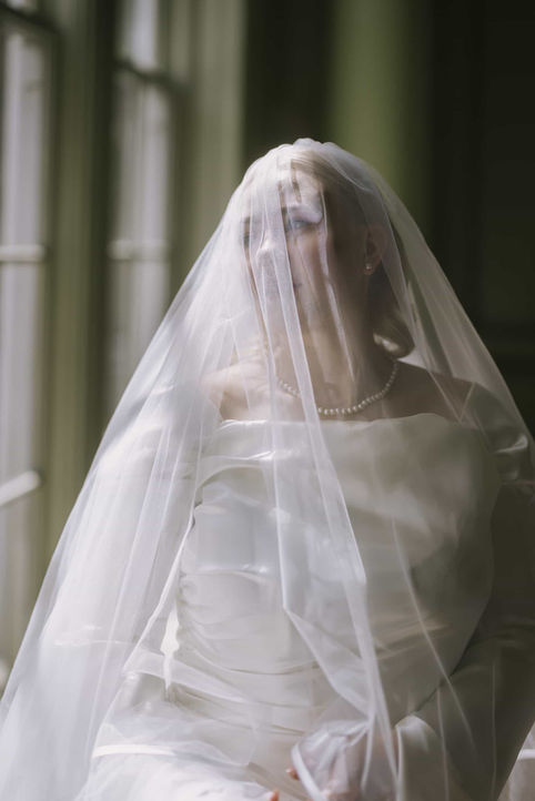 A soft, ethereal close-up portrait of a bride with a delicate sheer veil draped over her face.