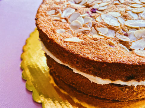 Side view of a berry bakewell cake. Flaked almonds on top and cream in the centre on a pink table
