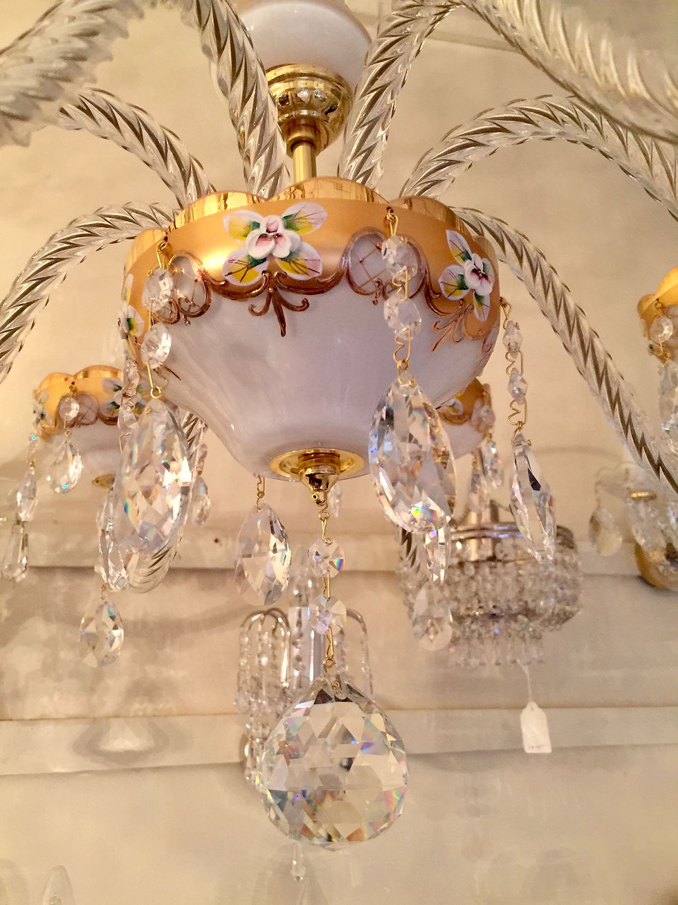 Thumbnail: Leona: A beautiful deep white elegant crystal chandelier with intricate clay flower details on a gold backdrop.