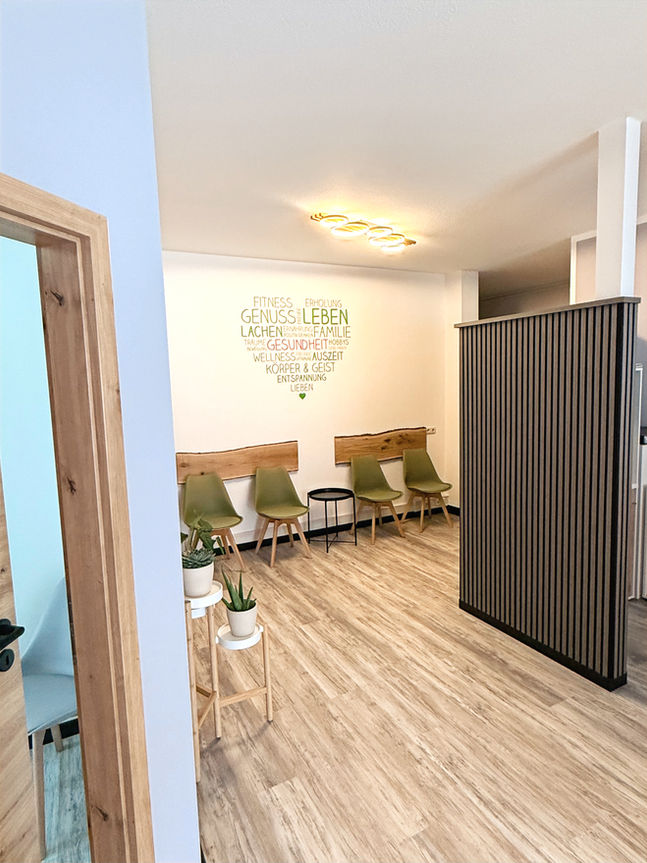 Modernes Wartezimmer in warmer Holzoptik mit Herz-Wandbild, das positive Begriffe wie Genuss, Leben, Lachen und Gesundheit zeigt.