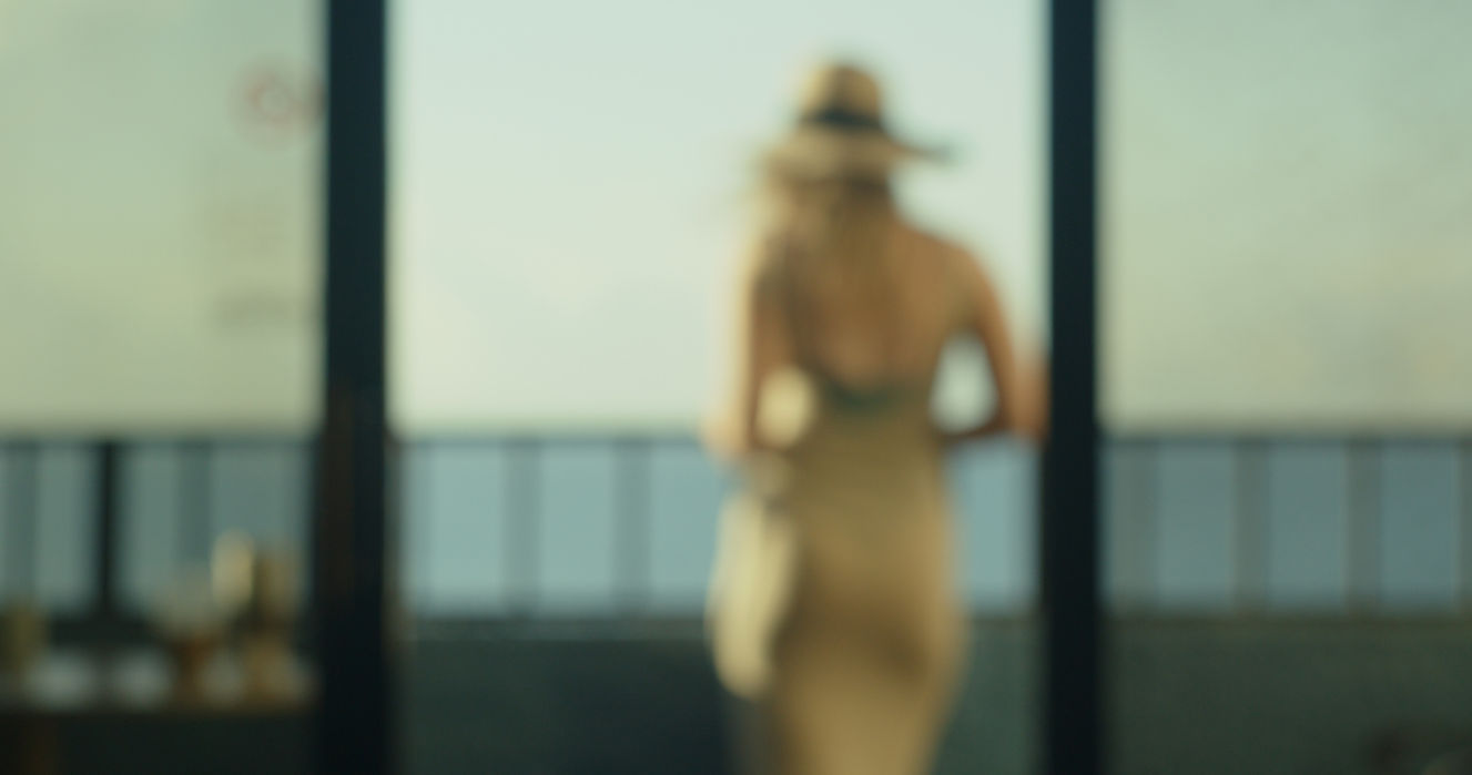 Blurred figure in a sundress and hat standing in an open doorway on an oceanview balcony