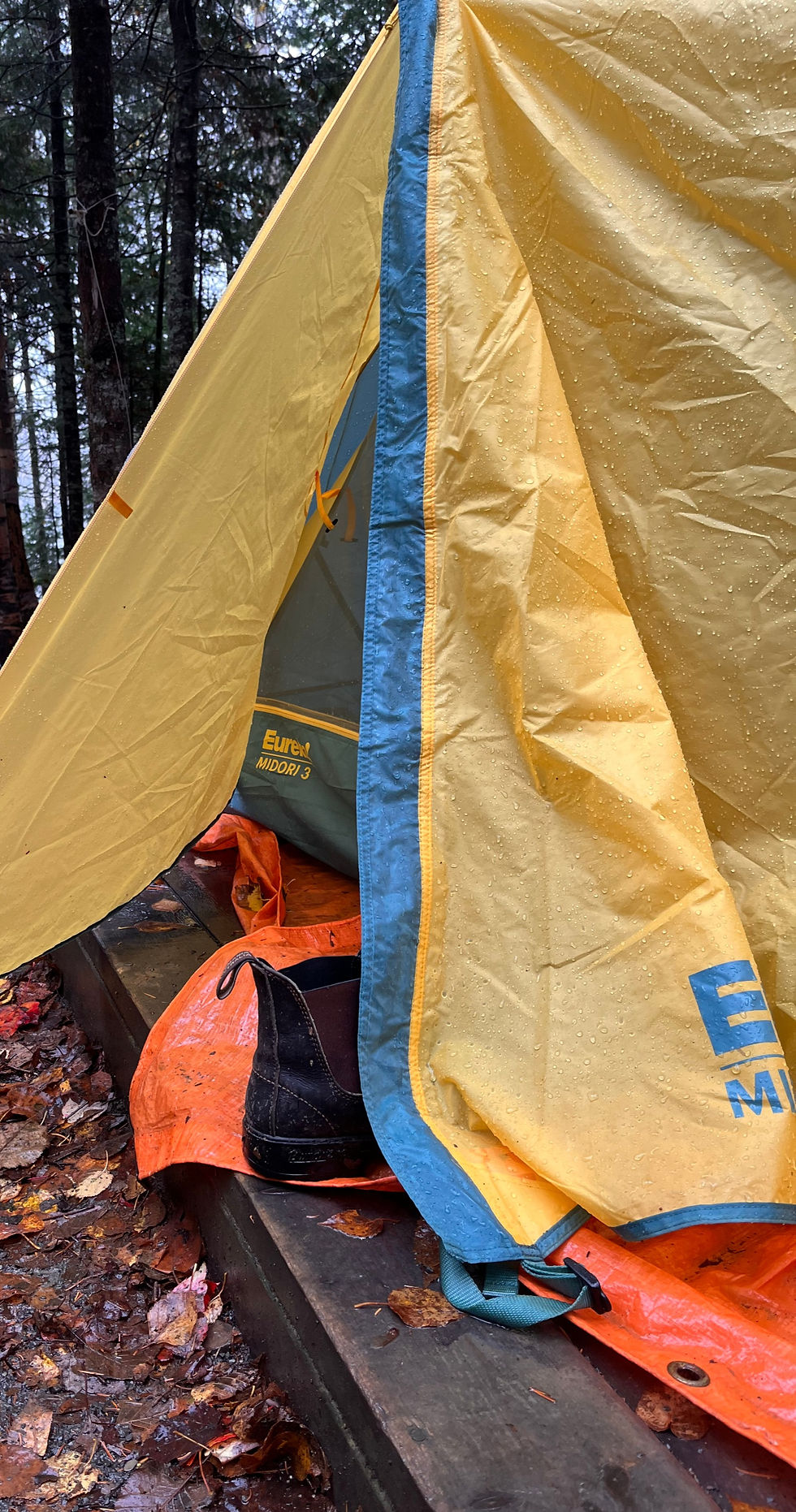 The door to a yellow tent is unzipped and a blundstone shoe sits outside the door on an orange tarp