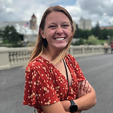 A woman in a orange shirt standing on a bridge and smiling.