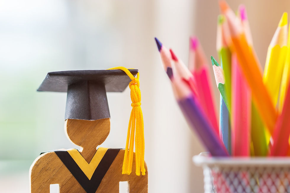 Wooden figure with a black graduation cap sits beside a cup of colorful pencils. Bright, cheerful mood with soft focus background.