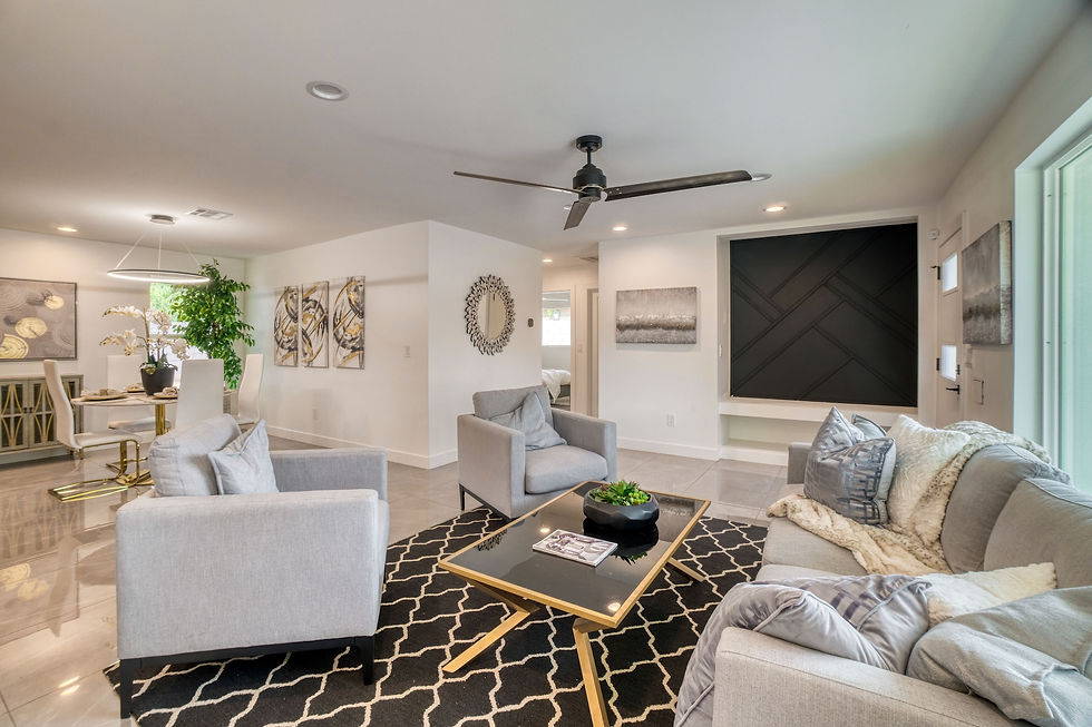 Modern living room with gray sofas, black and gold accents, geometric rug. Dining area visible, artwork on walls, bright and inviting.