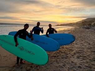 Three surfers holding Stormblade foam boards on the beach after a surf lesson in Malibu California at sunset