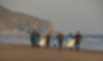 Group surf lesson students carrying surfboards on Broad Beach Malibu at sunset with Point Dume in background