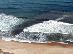 Rip current visible at Malibu beach with channel of water flowing out between breaking waves