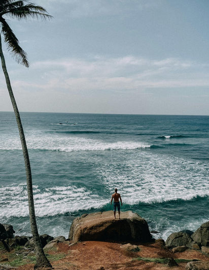 Surfer watching waves from a tropical coastline in Sri Lanka during an ocean adventure journey.