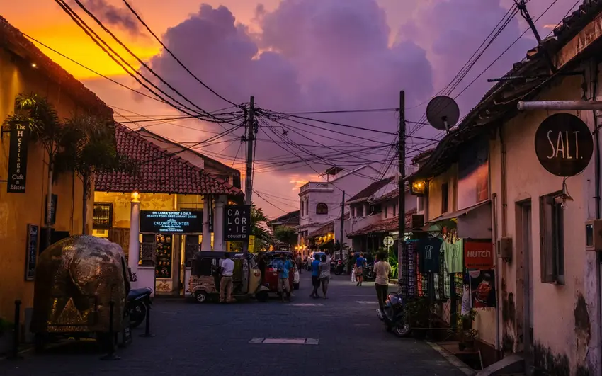 Atmospheric street inside Galle Fort at sunset with warm lights, tuk-tuks, and colonial architecture.
