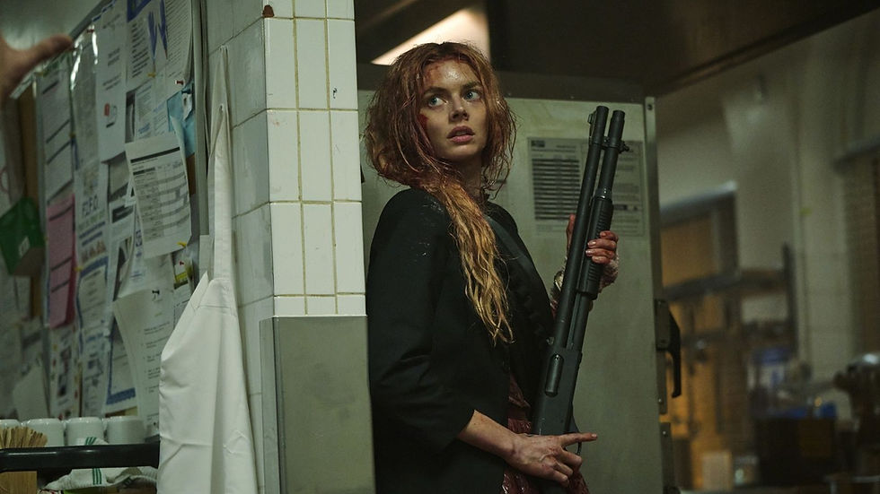 Woman with wet hair holds a shotgun in a tiled kitchen, looking alert. Papers and apron hang on the wall, creating a tense atmosphere.