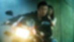 Tense man rides a Yamaha motorcycle in a green-lit tunnel while a worried woman clings to him from behind.