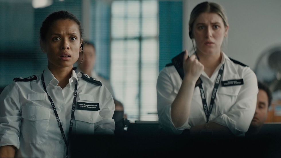 Two police officers in white uniforms look concerned in an office setting, wearing headsets and black lanyards. One name tag reads "Chief Superintendent."