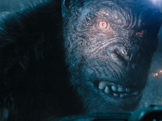 Close-up of a giant gorilla with glowing eyes and dark fur, set against a smoky, fiery background, creating a tense atmosphere.