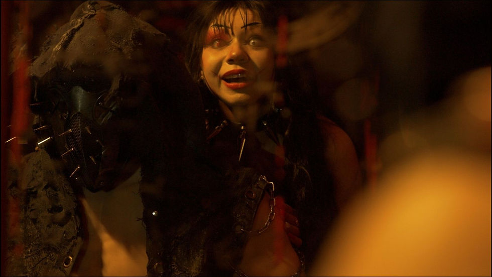 Two people in dim lighting, one wearing a spiked mask, the other with dramatic makeup. Moody and intense atmosphere with dark tones.