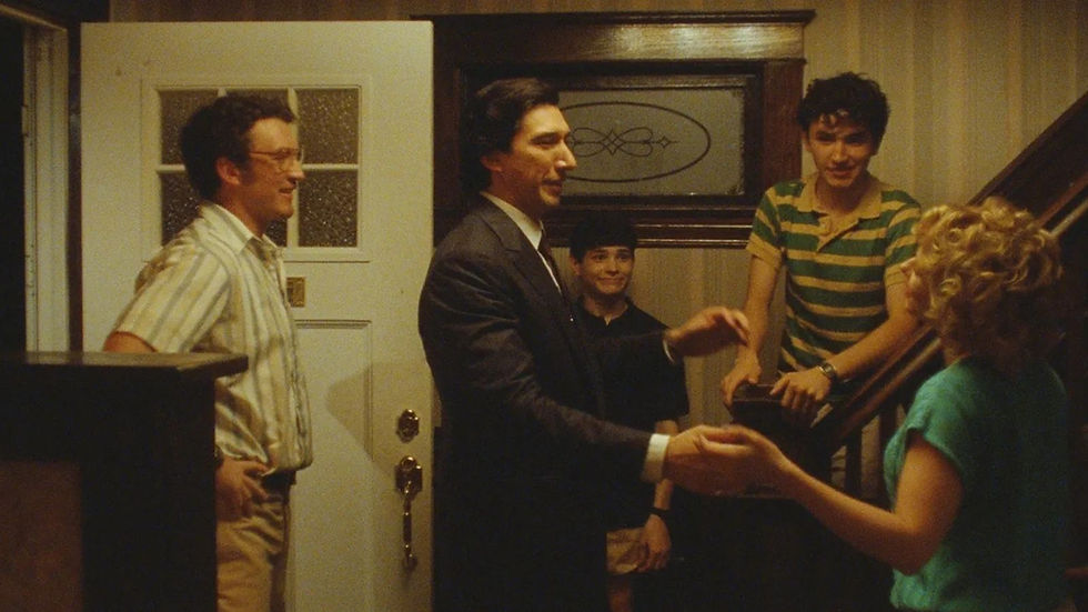 Five people in a warm-lit home entryway; a man in a suit shakes a woman’s hand while others smile by the stairs.
