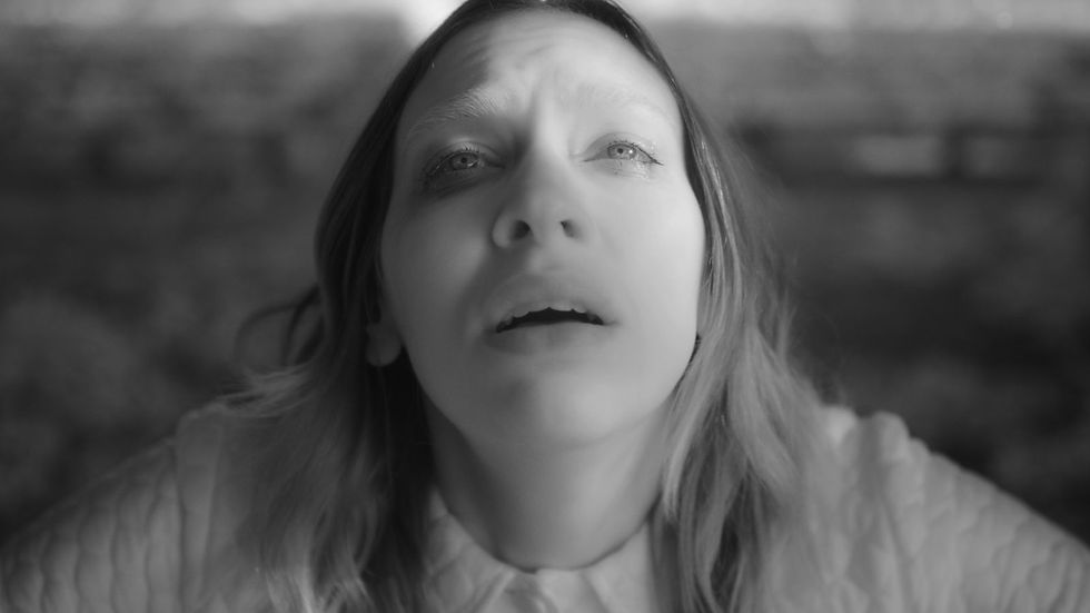 Black-and-white close-up of a woman looking upward with parted lips, against a blurred background, conveying awe or concern.