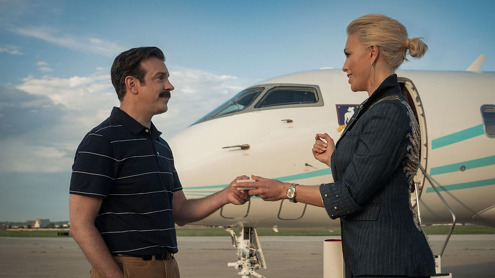 Man and woman exchange a small item beside a private jet on an airport tarmac, smiling under a blue sky.