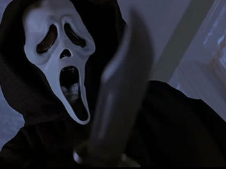 Masked figure in black robe holding knife indoors, against a blue-tinted background. The mask has a white, ghost-like face, evoking fear.