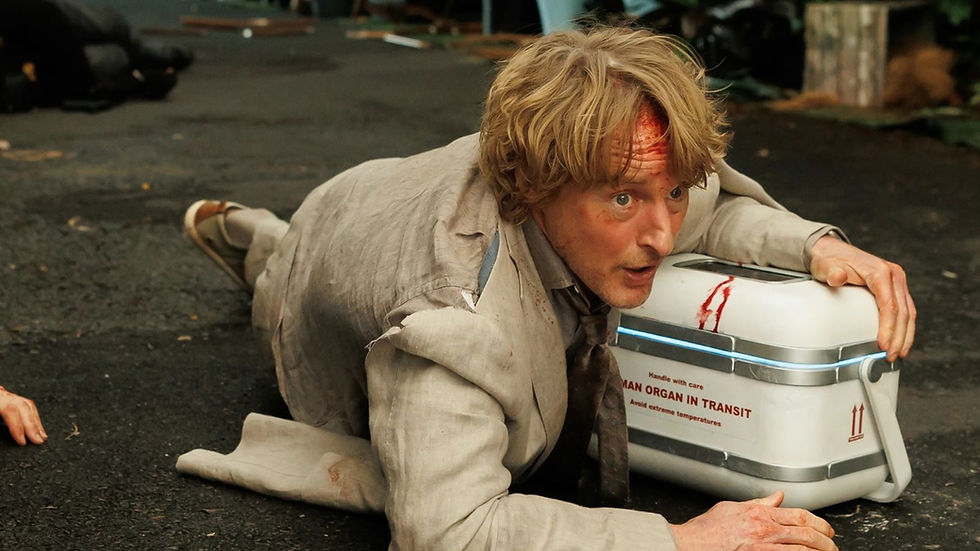 Injured blond man crawls on wet floor beside a white medical case labeled HUMAN ORGAN IN TRANSIT, looking tense and urgent.