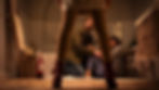 Low-angle view through a woman’s legs of a man kneeling to comfort a frightened woman in a tiled bathroom, tense mood.