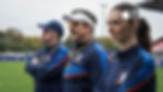 Three coaches in navy tracksuits stand on a sports field, watching intently; Apple TV logo at top right.