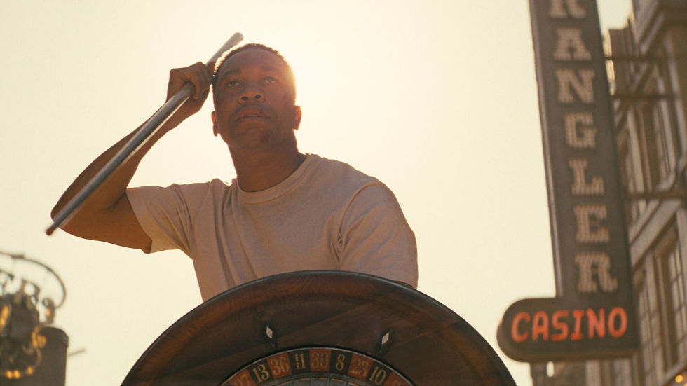 Man in a beige shirt spins a roulette wheel under a bright sky. Casino sign visible in the background. Intense mood.