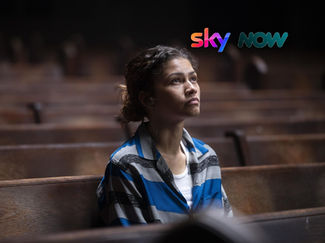 A person in a blue striped shirt sits alone on a wooden bench in a dimly lit space, looking contemplative and thoughtful.