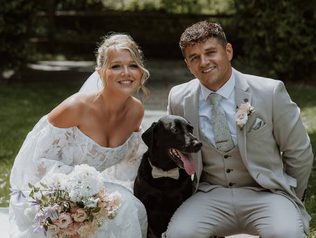Bride and groom with pastel wedding flowers posing with their sweet black labrador