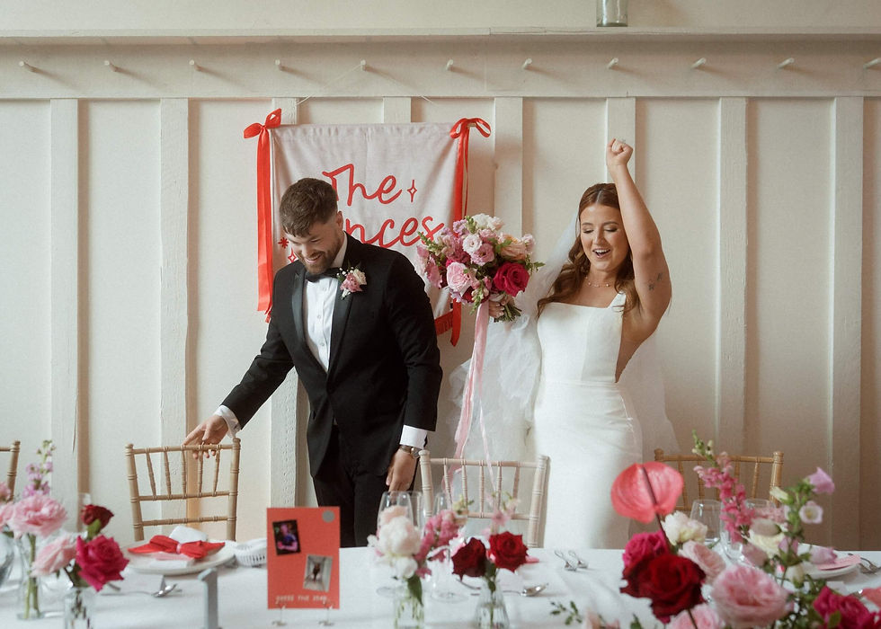 bride and groom joyfully sitting at their top table surrounded by pink and red wedding flowers