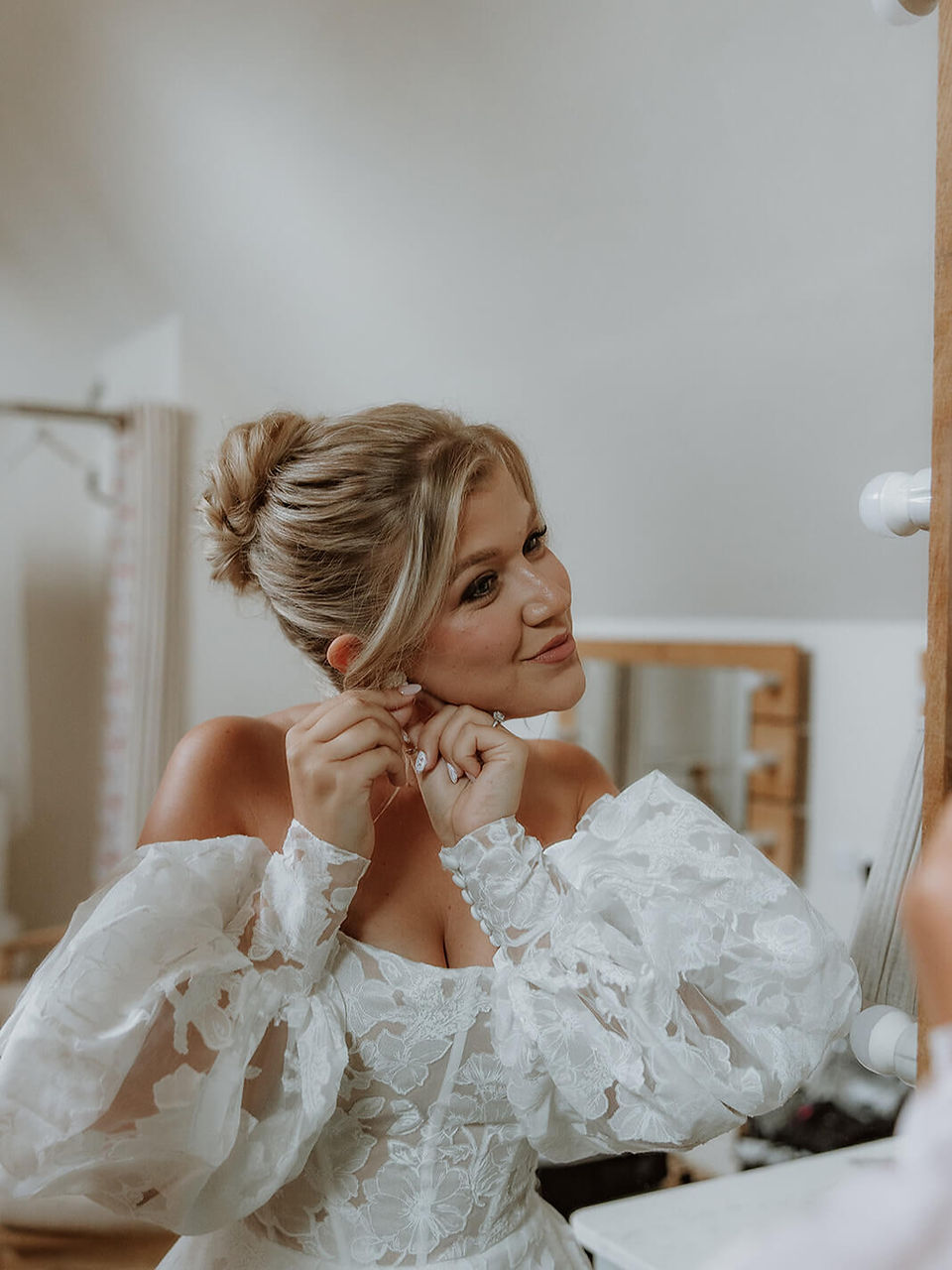 a stunning bride in an off-shoulder wedding dress putting her earrings on