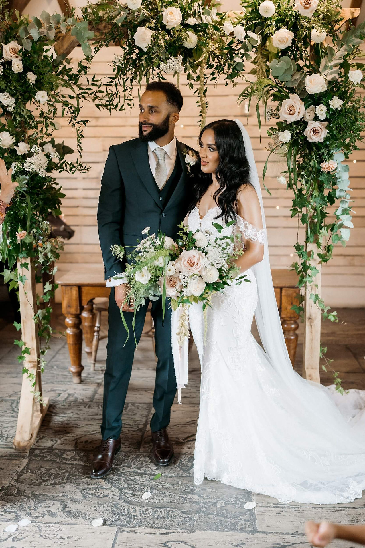 Bride and groom standing under a beautiful, untamed, green and white flower arch